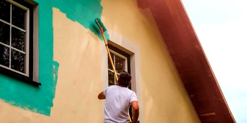 Un ouvrier peint les murs de la façade d'une maison avec de la peinture
