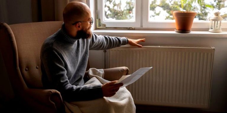Homme sous une couette à côté d'un radiateur