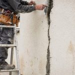 Artisan rebouchant une fissure de façade en enduit sur un mur extérieur